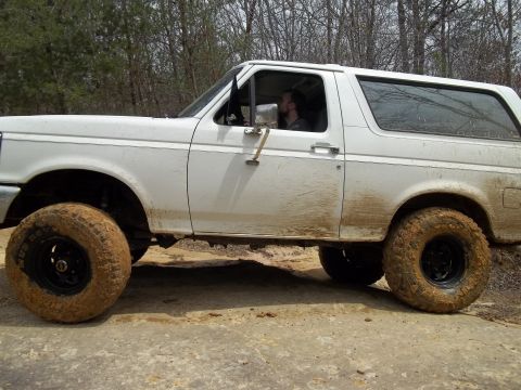 1990 Ford Bronco - A white Ford Bronco is shown driving off-road, covered in mud.