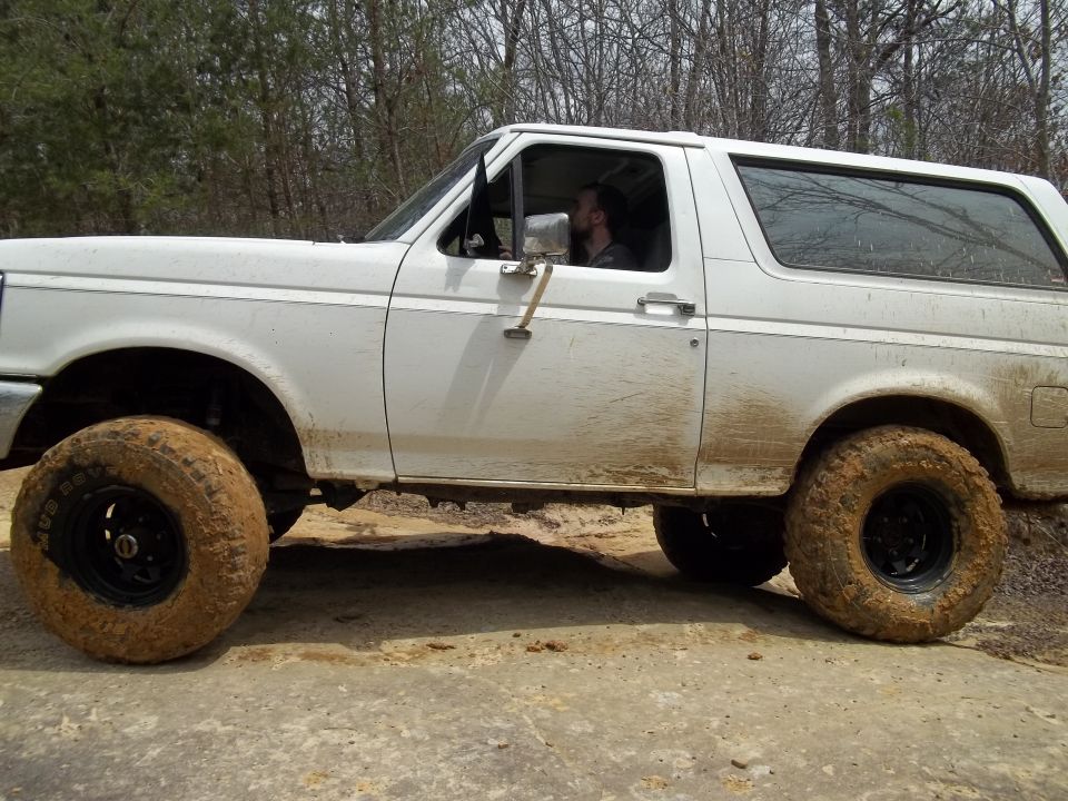White Ford Bronco with mud on tires driving on a dirt road