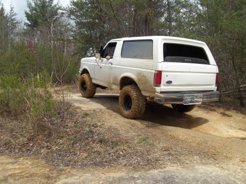 1990 Ford Bronco - This 1990 Ford Bronco is captured in a three-quarter front view as it navigates a muddy off-road path.