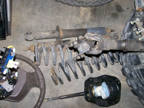1988 Suzuki Samurai - Various automotive parts, including suspension components and a steering wheel, are displayed on a concrete surface.