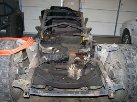 1988 Suzuki Samurai - The chassis of a 1988 Suzuki Samurai is shown with large off-road tires and orange cables, indicating a project vehicle.