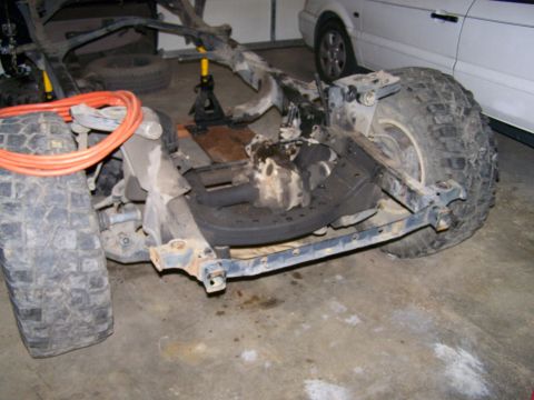 1988 Suzuki Samurai - The frame and suspension of a vehicle are visible, with large tires and some components on jack stands.