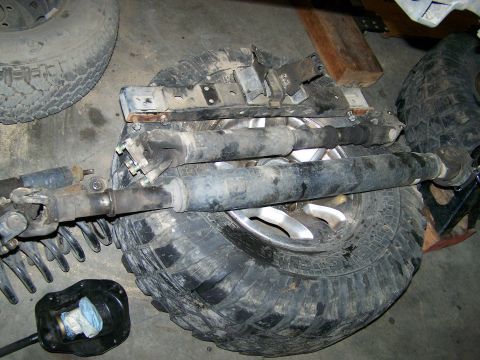 1988 Suzuki Samurai - Driveshafts and tires are laid out on a garage floor, with a black transfer case boot in the foreground.