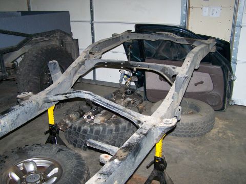 1988 Suzuki Samurai - The frame of a vehicle is shown on jack stands, with spare tires and doors nearby, suggesting a project or repair.