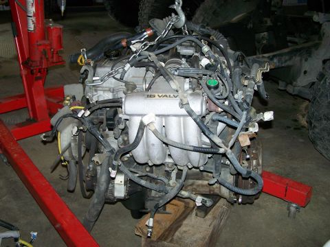 1988 Suzuki Samurai - An engine is being worked on, suspended by a chain hoist and supported by a wooden block.