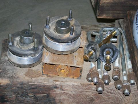 1988 Suzuki Samurai - Two spring spacers and multiple U-bolts are laid out on a wooden surface, likely for a vehicle modification.