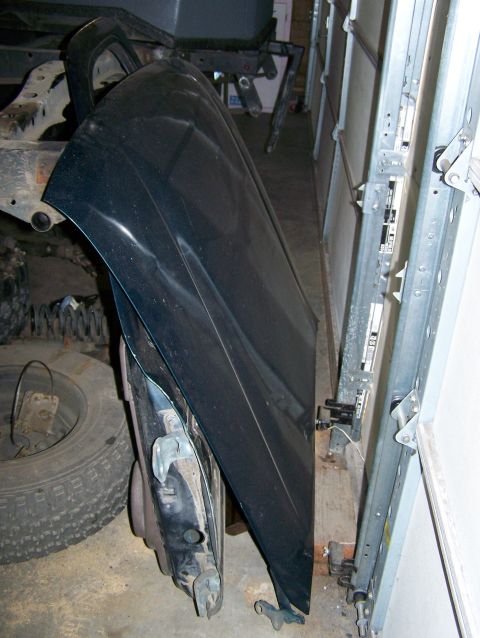 1988 Suzuki Samurai - A black fender and a tire are visible in a garage setting, leaning against a metal track.