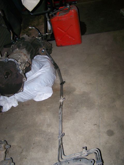 1988 Suzuki Samurai - Transmission and fuel lines are laid out on a concrete floor next to a red gas can.
