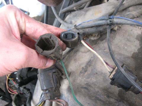1981 Ford Bronco - A hand disconnects electrical connectors in a vehicle's engine bay, showing various wires and cables.