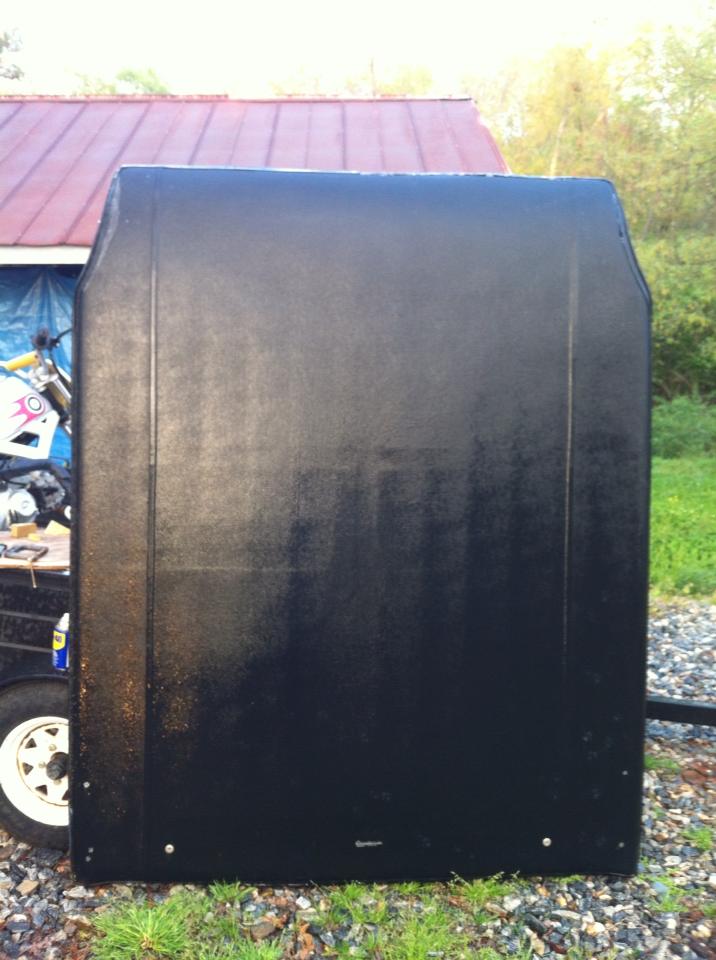 Black hood resting on a trailer, with a motorcycle and building in the background