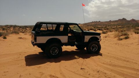 1994 Ford Bronco - A modified Ford Bronco sits in a desert landscape under a cloudy sky, with a prominent orange flag flying.