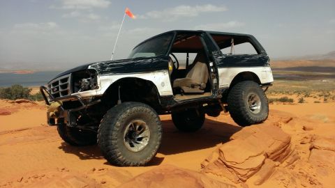 1994 Ford Bronco - Modified 1994 Ford Bronco navigates a rocky desert terrain with a clear sky overhead.