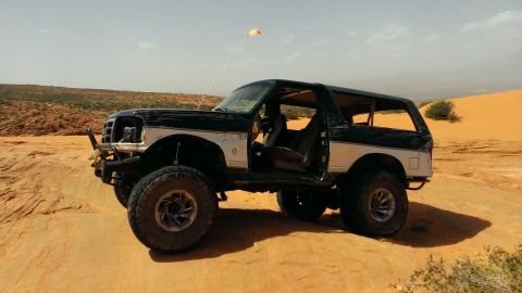 1994 Ford Bronco - Modified Ford Bronco sits on a sandy terrain under a clear sky.