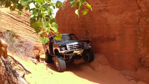 1994 Ford Bronco - This modified Ford F-Series truck is driving through a tight, sandy canyon with red rock walls.