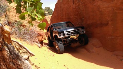 1994 Ford Bronco - A black Ford Bronco navigates a narrow, sandy canyon with steep, orange rock walls.