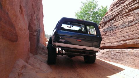 1994 Ford Bronco - A dark blue 1994 Ford Bronco navigates a tight passage between towering red rock formations.