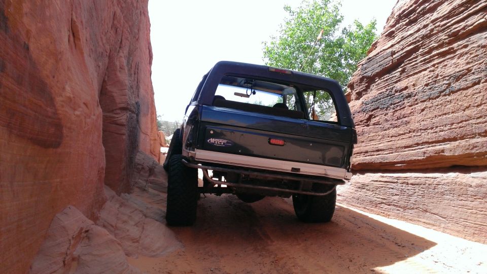 Dark blue 1994 Ford Bronco driving through a narrow canyon with red rock walls