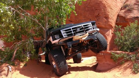 1994 Ford Bronco - Modified black Ford Bronco navigates a challenging off-road trail with steep inclines and rocky terrain.