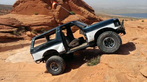 1994 Ford Bronco - A Ford Bronco navigates a rocky, off-road terrain with a body of water in the background.