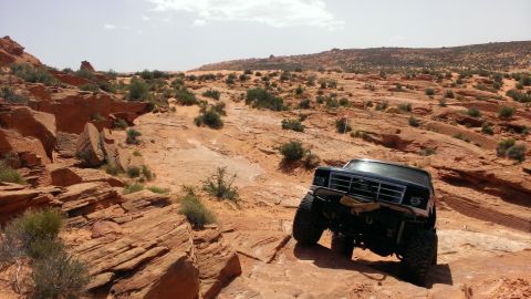 1994 Ford Bronco - A black 1994 Ford Bronco navigates a challenging off-road path in a desert landscape.