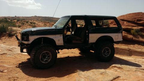 1994 Ford Bronco - This modified Ford Bronco is shown off-road with its doors open, parked on desert rocks.