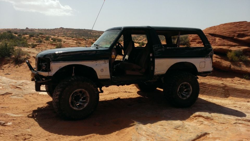 Modified Ford Bronco parked on rocky desert terrain. Doors are open