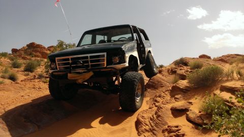 1994 Ford Bronco - Modified Ford Bronco navigates a steep, sandy desert trail with its driver's door ajar.