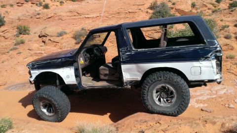 1994 Ford Bronco - This 1994 Ford Bronco shows significant damage to its body panels while navigating a , sandy landscape.
