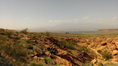 1994 Ford Bronco - A vast desert landscape unfolds, with rocky terrain and a body of water visible on the horizon under a pale sky.