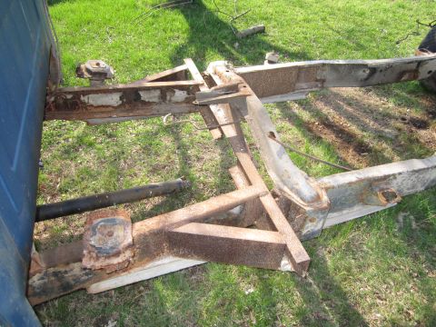 1986 Jeep Grand Wagoneer - The underside of a vehicle's frame, showing significant rust and wear, sits on grass.