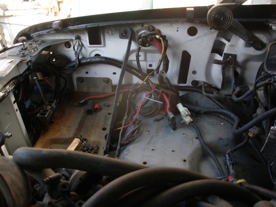 Stripped engine bay firewall with exposed wiring, cables, and a firewall-mounted relay/solenoid.