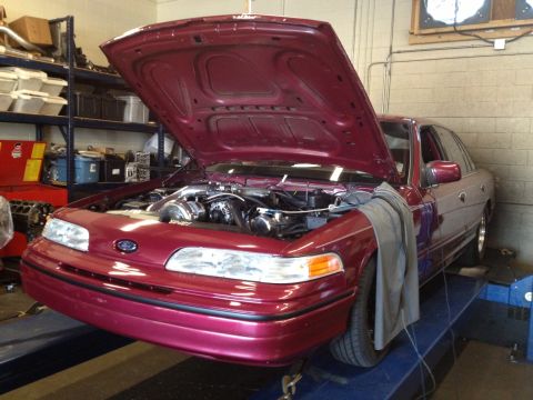 1992 Ford Crown Victoria - A maroon 1992 Ford Crown Victoria is positioned on a dynamometer with its hood open, revealing the engine bay.