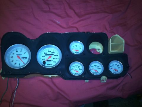 1973 Ford Ranchero - An automotive instrument cluster with multiple gauges is displayed against a red background.