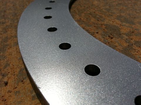 1995 Ford Bronco - A silver wheel spacer with a row of bolt holes is shown against a textured background.