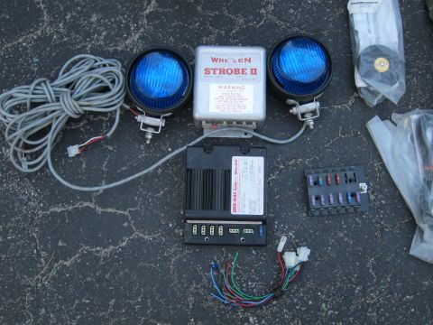1991 Ford LTD Crown Victoria - Components of a Whelen strobe light system, including the control box, lights, and fuse block, laid out on asphalt.