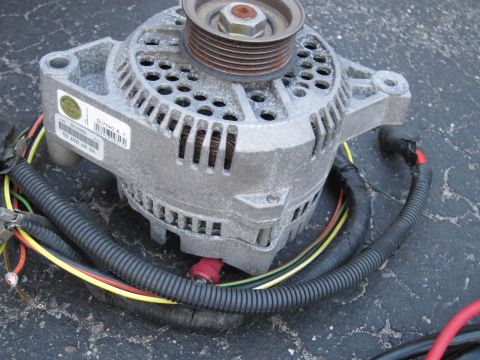 1991 Ford LTD Crown Victoria - A car alternator with a pulley and electrical wiring is shown close-up on a dark surface.