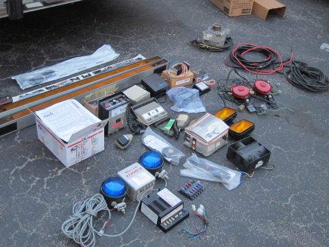 1991 Ford LTD Crown Victoria - Assorted police equipment, including strobes, sirens, and control units, are spread across an asphalt surface.