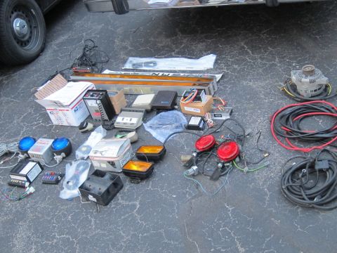 1991 Ford LTD Crown Victoria - Various police car parts are spread out on a cracked asphalt surface, including lights, a siren, and electrical components.