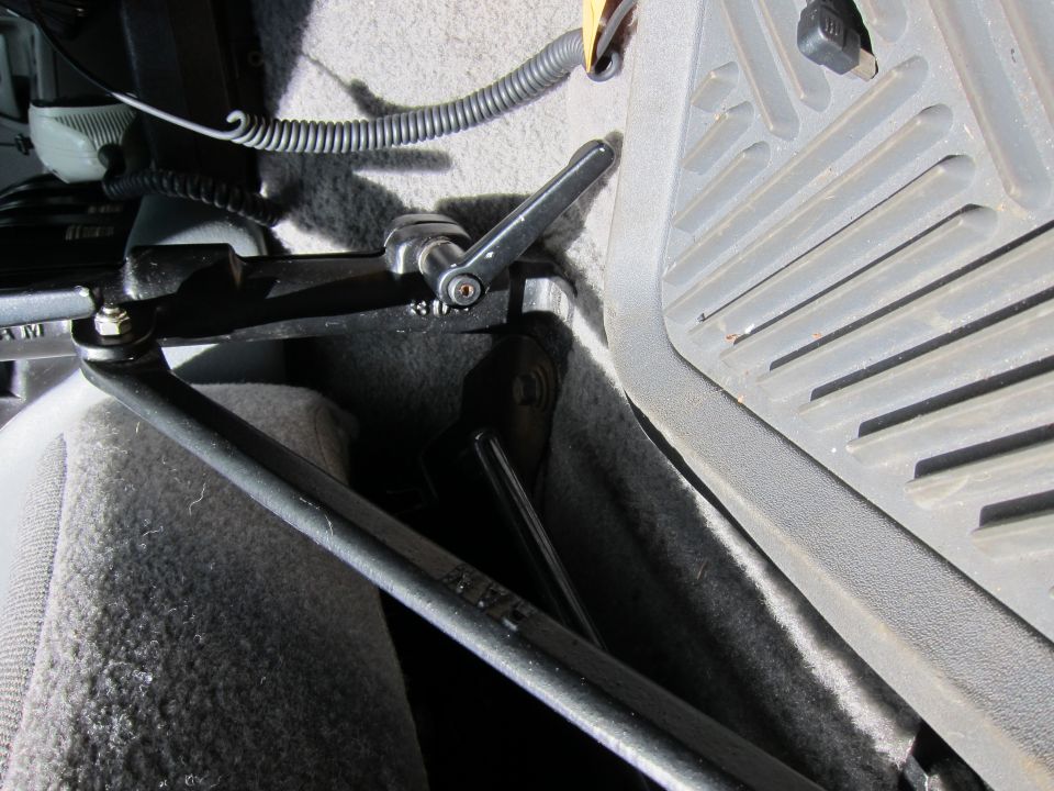 Close-up of a black metal bracket with a lever attached, mounted to a car's interior floor