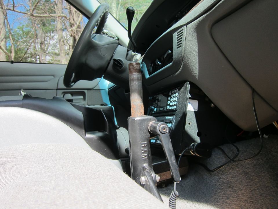 Car interior showing steering wheel, dashboard, and a RAM mount device. Aftermarket radio and other equipment are visible