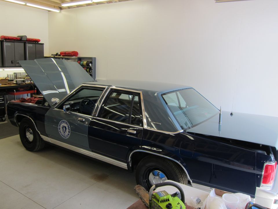 1991 Ford Crown Victoria LTD police car with hood open, parked in a garage with equipment in the background