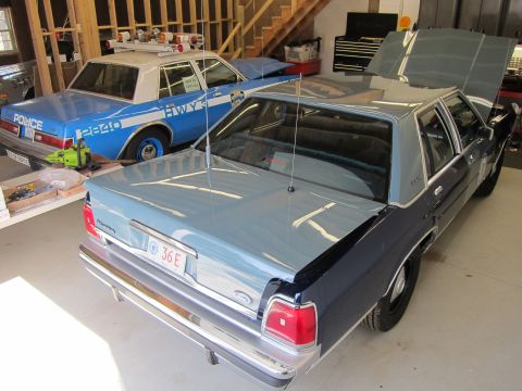 1991 Ford LTD Crown Victoria - Two police cars are parked inside a garage, one with its hood open.