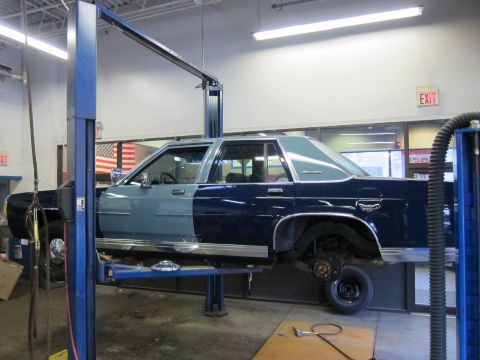 1991 Ford LTD Crown Victoria - A two-tone 1991 Ford Crown Victoria LTD is seen on a car lift in a garage, with its wheels removed for maintenance.