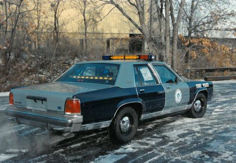 1991 Ford LTD Crown Victoria - Police car with light bar on roof, driving on snowy road. State Police markings visible.