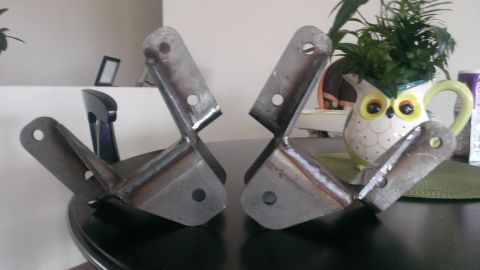1994 Ford Bronco - Two custom metal brackets are displayed on a table, with household items in the background.