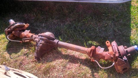1979 Ford Bronco - This is a rusty front axle assembly, likely from an older vehicle, resting on grass.
