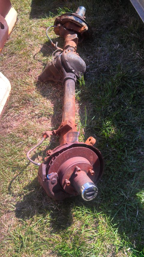 1979 Ford Bronco - A rusty front axle assembly with disc brakes and a hub is shown resting on a grassy surface.