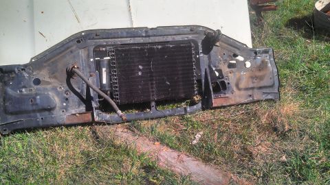1979 Ford Bronco - A disassembled radiator support with condenser unit rests on the grass, showing signs of rust and wear.