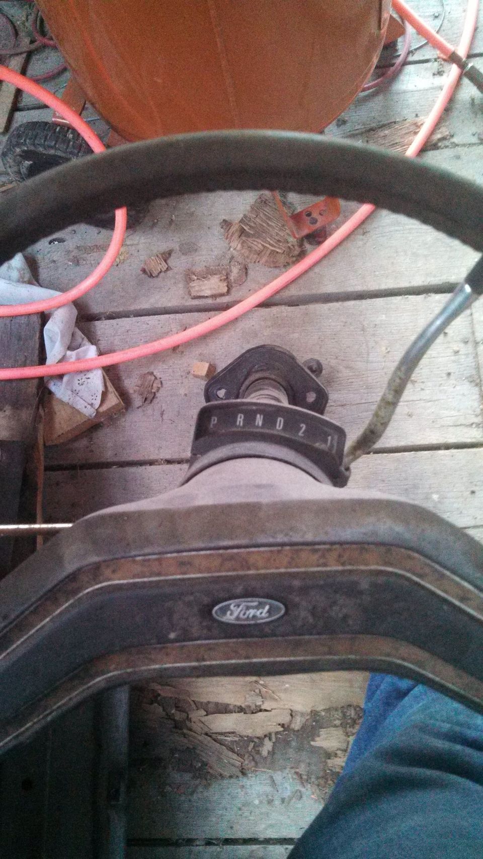 Ford steering wheel, column shifter with PRND2 markings, and dashboard trim. Floorboards visible