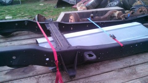 1979 Ford Bronco - A disassembled truck frame with suspension components is strapped down on a wooden deck.
